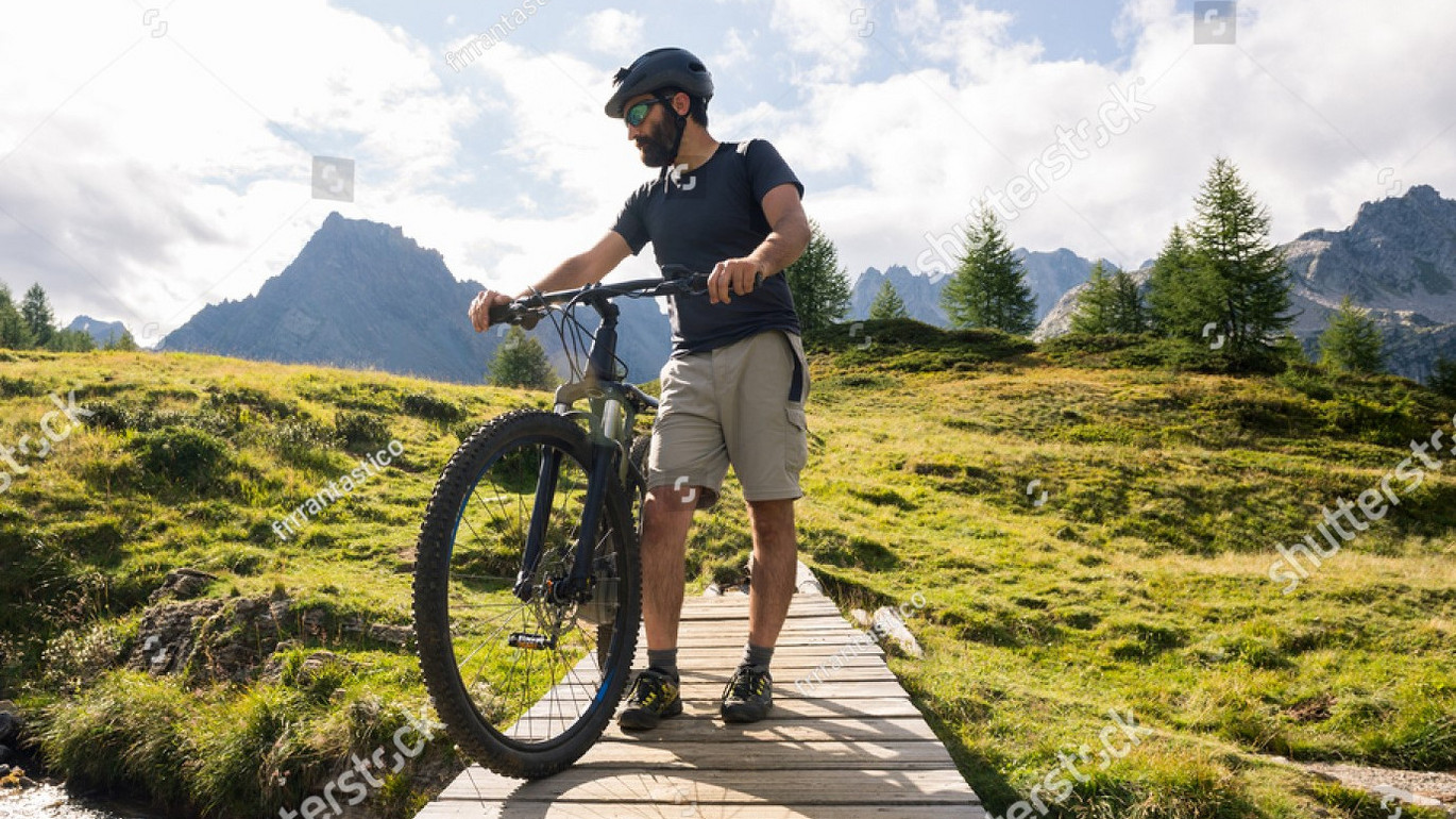 Stock-photo-young-adult-active-man-on-wooden-little-bridge-on-mountain-wearing-bike-helmet-looking-at-river-721436398