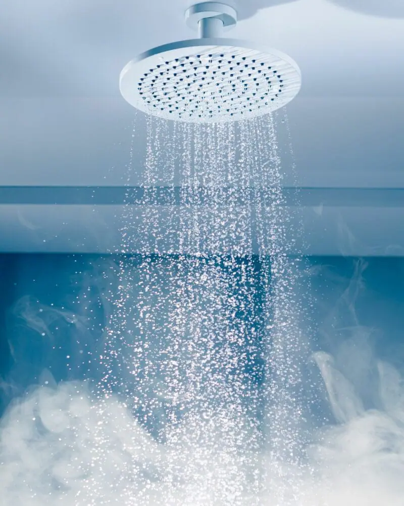 Wasserstrahl aus einer Decken-Regendusche mit feinem Sprühbild und aufsteigendem Dampf